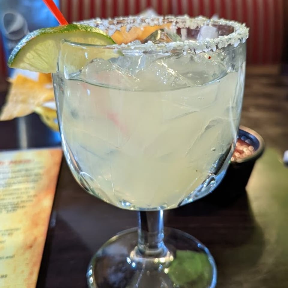 A La Parrilla margarita with a salted rim, lime wedge, and red straw.