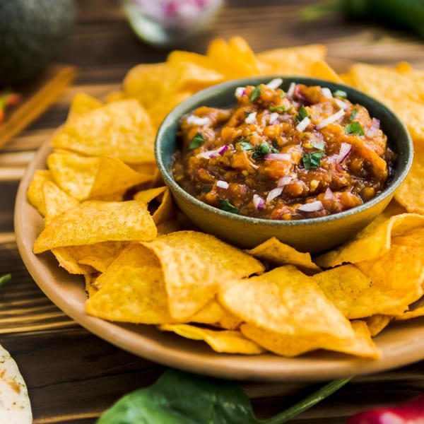A bowl of La Parrilla's fresh Mexican salsa with chopped onions and cilantro, surrounded by tortilla chips.