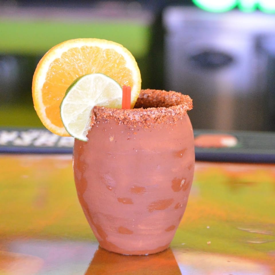 A La Parrilla Mexican drink in a clay mug, garnished with orange and lime slices.