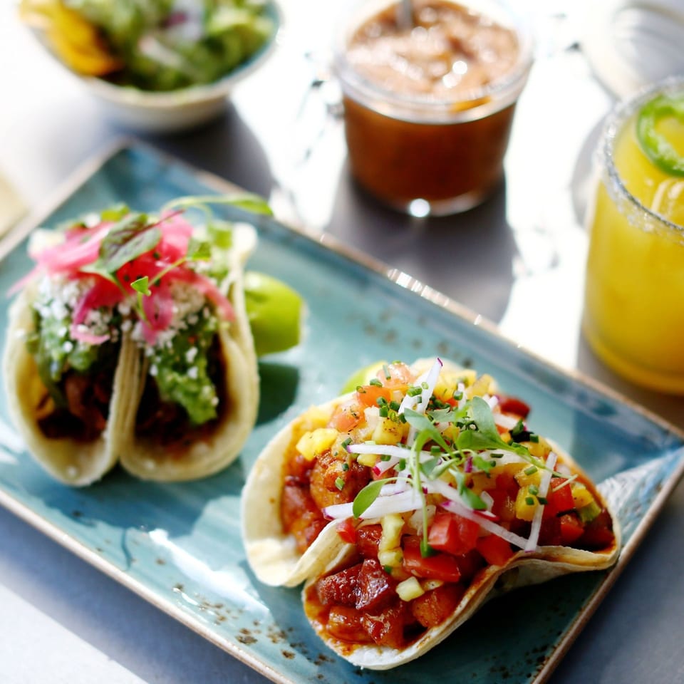 Two La Parrilla Fresh Mexican tacos with various toppings, salsa, and a margarita on a blue plate.